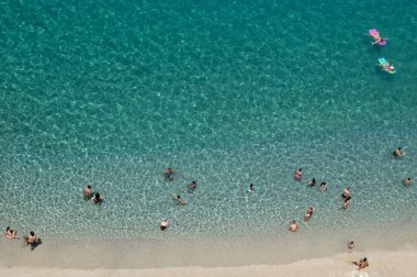 Yazın şeffaf mavi suyla yüzen insanların olduğu kumlu sahil manzarası. Üst Manzara. Peyzaj