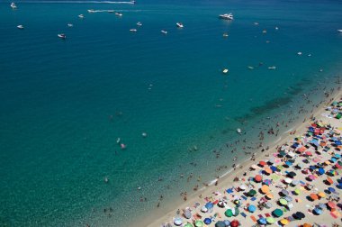 Yazın şeffaf mavi suyla yüzen insanların olduğu kumlu sahil manzarası. Üst Manzara. Peyzaj