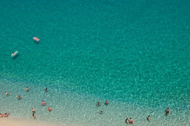 Yazın şeffaf mavi suyla yüzen insanların olduğu kumlu sahil manzarası. Üst Manzara. Peyzaj