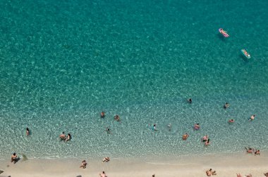 Yazın şeffaf mavi suyla yüzen insanların olduğu kumlu sahil manzarası. Üst Manzara. Peyzaj