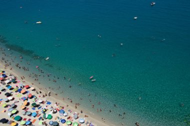 Yazın şeffaf mavi suyla yüzen insanların olduğu kumlu sahil manzarası. Üst Manzara. Peyzaj