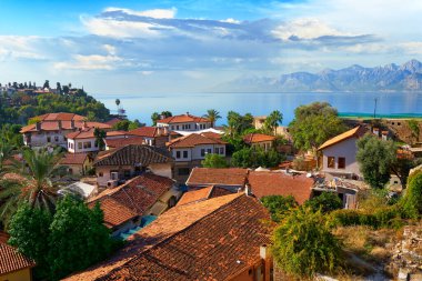 Colorful private houses with orange roofs among tropical greenery against the backdrop of the picturesque Mediterranean Sea and mountains in the city of Antalya, Turkey                              