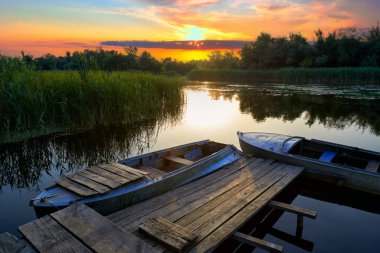 Günbatımında Dinyeper Deltası 'ndaki sazlıklar arasında eski bir ahşap iskele ve eski teknelerle dolu görkemli bir manzara. Dinyeper Nehri, Konka Nehri, Kherson Bölgesi, Ukrayna