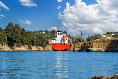 Tanker Corinth Kanalı 'nın kayalıklarının arasından geçiyor. Parlak güneşli bir günde beyaz bulutlu mavi gökyüzüne karşı Corinth Kanalı 'nın manzaralı yaz manzarası. Moreloponez, Yunanistan                               