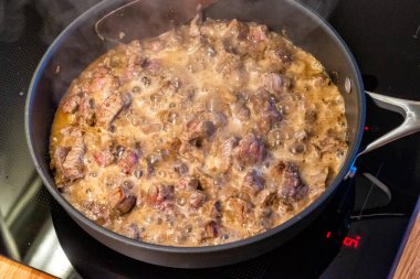 Et bir tavada pişiriliyor, et taşlama işlemi yapılıyor.