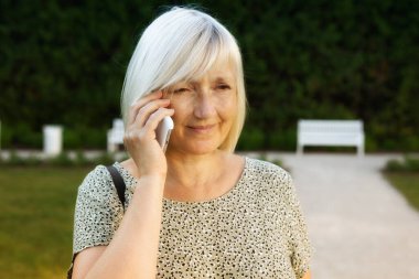 Kadın parkta cep telefonuyla konuşuyor.