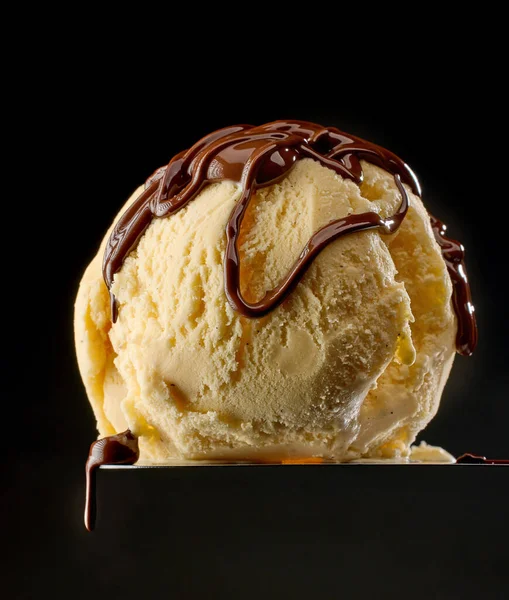 melted chocolate on vanilla ice cream ball on black background