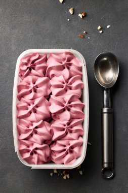 open box of pink ice cream and spoon on dark grey background, top view