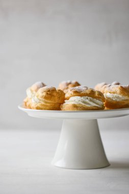 plate of cream puffs decorated with powdered sugar on light grey background