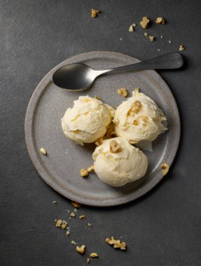 plate of vanilla ice cream decorated with walnuts on grey background, top view