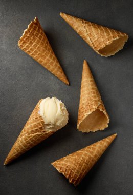 vanilla ice cream and waffle cones on dark grey background, top view
