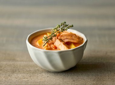 bowl of salmon and tomato soup decorated with fresh thyme on wooden kitchen table