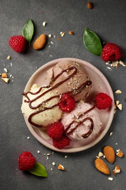 various ice cream balls on pink plate decorated with chocolate sauce and fresh berries, top view