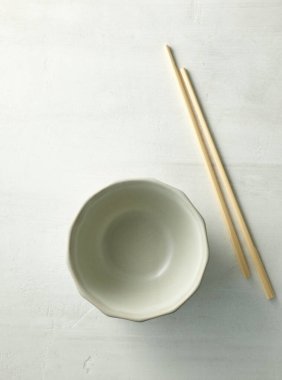 empty bowl and chopsticks on light kitchen table, top view