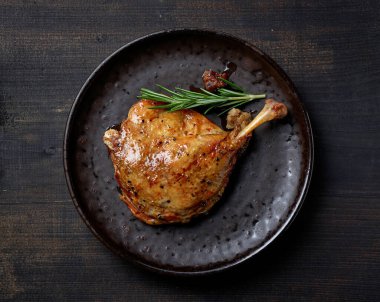 plate of duck leg confit on black table, top view