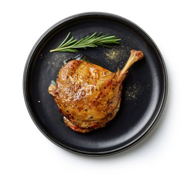 duck leg confit on black plate isolated on white background, top view