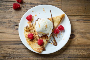 Krep, ahşap masada dondurma ve ahududu ile süslenmiş.