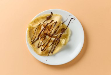 Beyaz tabakta erimiş çikolata sosuyla süslenmiş taze pişmiş krep.