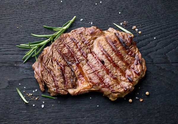 Freshly grilled beef entrecote steak on black wooden board, top view