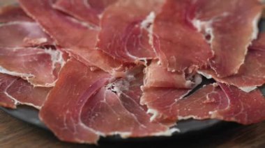 Bir tabak dilimlenmiş İspanyol Iberico jambonu ahşap masa arkasında, dönüyor.