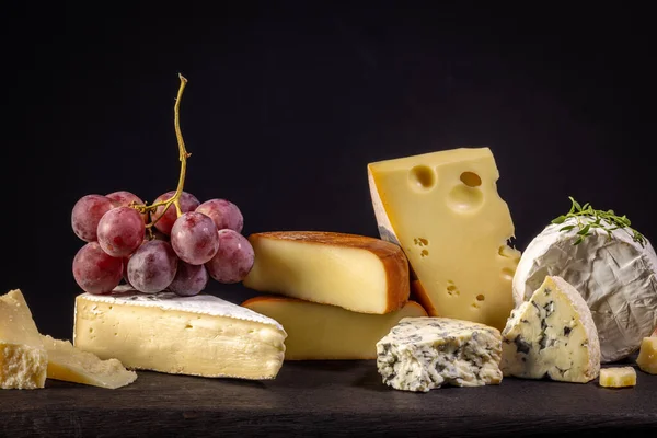 Stillleben Mit Verschiedenen Käsesorten Und Trauben Auf Schwarzem Hintergrund — Stockfoto
