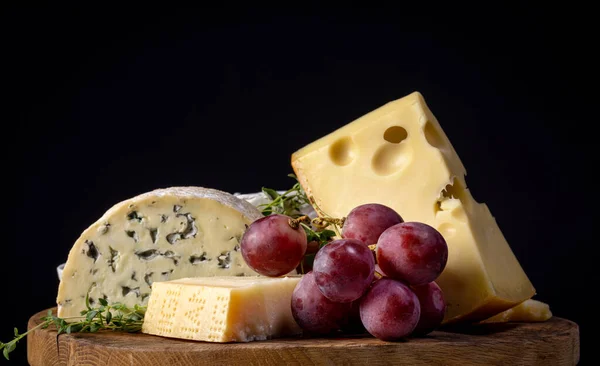 木の板や黒の背景にチーズやブドウがたくさん残っています — ストック写真