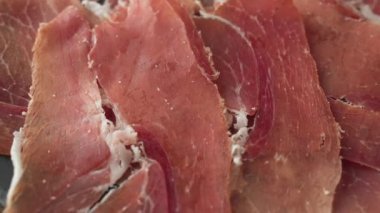 Bir tabak dilimlenmiş İspanyol Iberico jambonu ahşap masa arkasında, dönüyor.