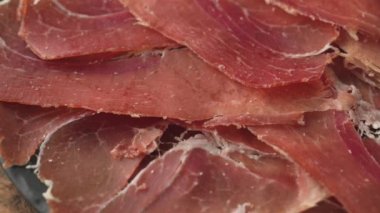Bir tabak dilimlenmiş İspanyol Iberico jambonu ahşap masa arkasında, dönüyor.