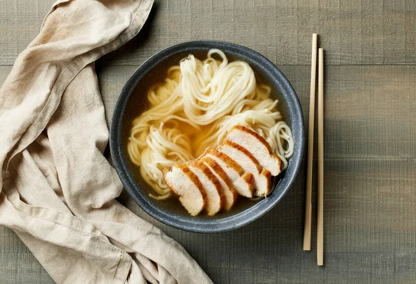 木のテーブルにチキンフィレット肉とアジア麺スープのボウル トップビュー — ストック写真