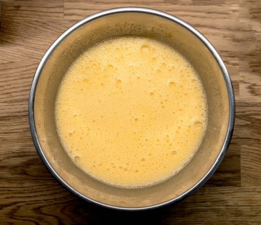 Ahşap mutfak masasında metal kasede çırpılmış yumurta, üst manzara.