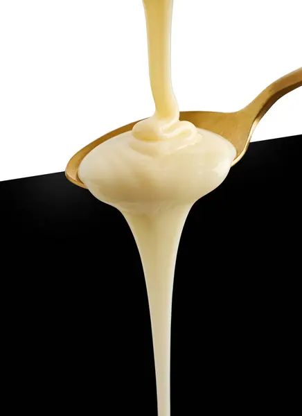黒と白の背景に黄金のスプーンに注ぐ凝縮ミルク — ストック写真