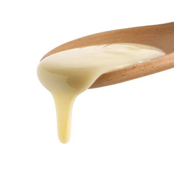 在白色背景上隔离的木制勺子中的浓缩牛奶 — 图库照片