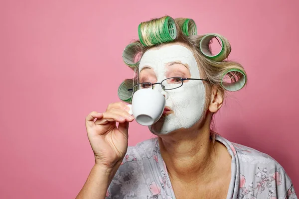 早上带着粘土面罩和发卷喝咖啡的有趣的老年妇女 — 图库照片