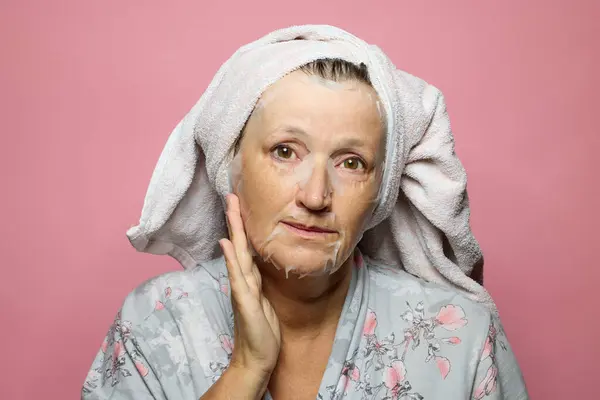老年妇女在粉红背景上使用湿面膜餐巾 — 图库照片