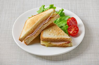 Kahvaltı masasında bir tabak jambon ve peynirli tost ve sebze.