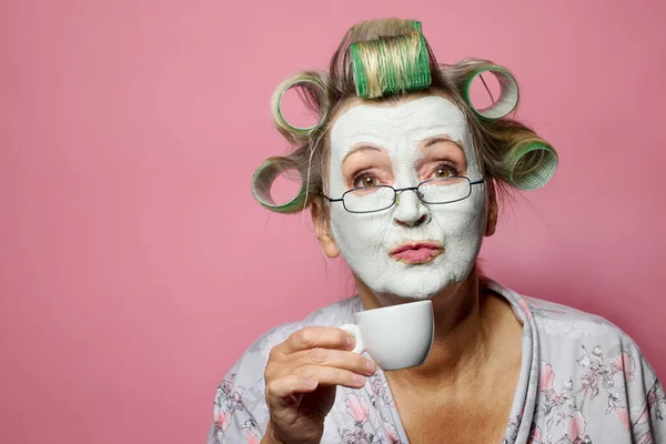 早上带着粘土面罩和卷发的有趣的老年妇女喝咖啡 — 图库照片