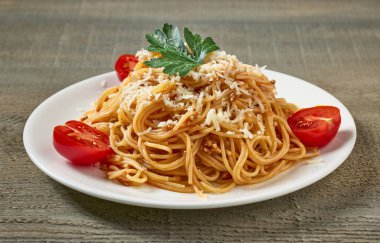 Bolonez soslu spagetti tabağı ve ahşap mutfak masasında domates.