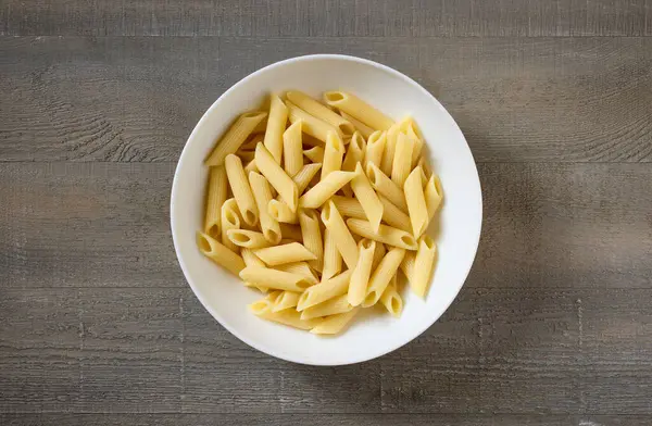 bowl of boiled pasta penne on wooden kitchen table, top view