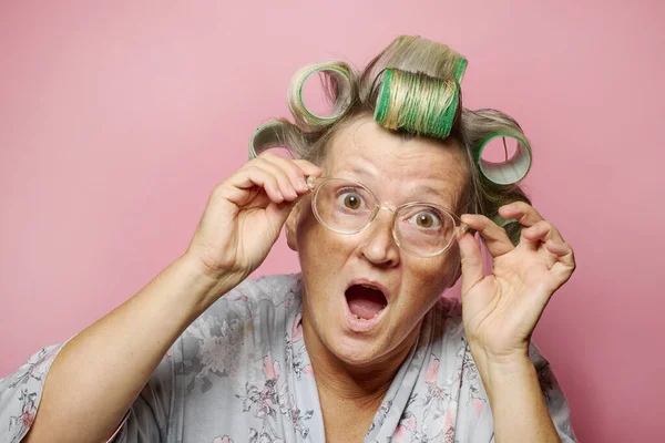 穿着粉色背景的发卷和眼镜的老年女性很惊讶 — 图库照片
