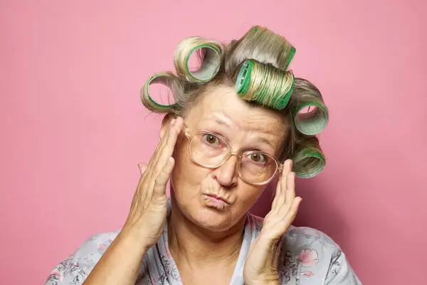 穿着粉色背景的发卷和眼镜的老年女性很惊讶 — 图库照片