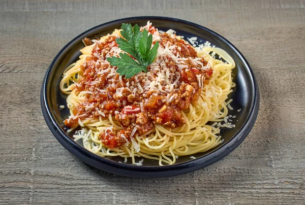 spaghetti with sauce bolognese on black plate on wooden kitchen table