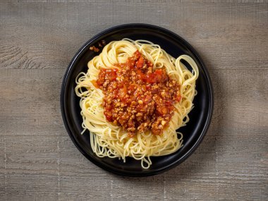 Eski ahşap mutfak masasında bir tabak spagetti bolonez.