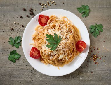 Bolonez soslu spagetti tabağı ve ahşap mutfak masasında domatesler.