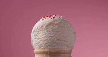 Dekoratif şeker parçacıklarının pembe arka planda dondurma topunun üzerine düşmesi, yavaş çekim videosu