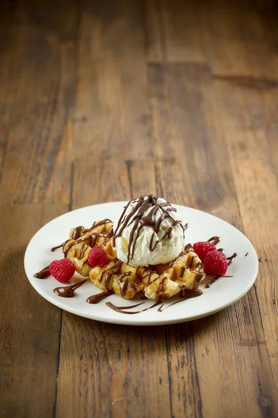 バニラアイスクリームとベルギーワッフルのプレート 木のテーブルにチョコレートソースとラズベリーを溶かした ロイヤリティフリーのストック画像