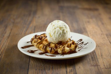 Vanilyalı waffle tabağı, ahşap masada erimiş çikolata sosu.