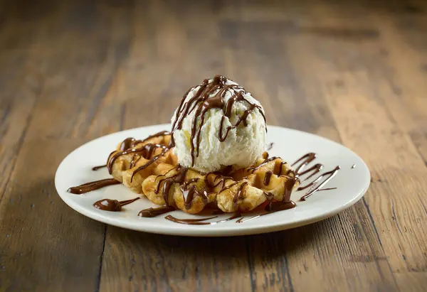バニラアイスクリームと溶けたチョコレートソースを木のテーブルに入れたベルギーワッフルのプレート ロイヤリティフリーのストック画像