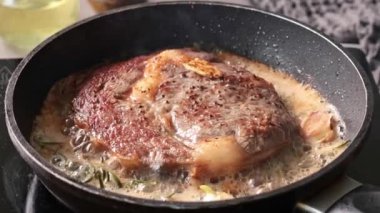 Erimiş tereyağında sarımsaklı ve biberiyeli bir tavada pişirilmiş lezzetli sığır eti eti. Evde mükemmel biftek yapma süreci.