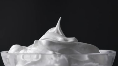 Şef cam bir kaseden kaşıkla çırpılmış yumurta beyazı ve şeker alır. Siyah arka planda yiyecek yakın plan