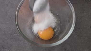 Aşçı, cam kasede çiğ yumurta sarısına kaşıkla şeker ekler. Yiyeceklere yakın çekim